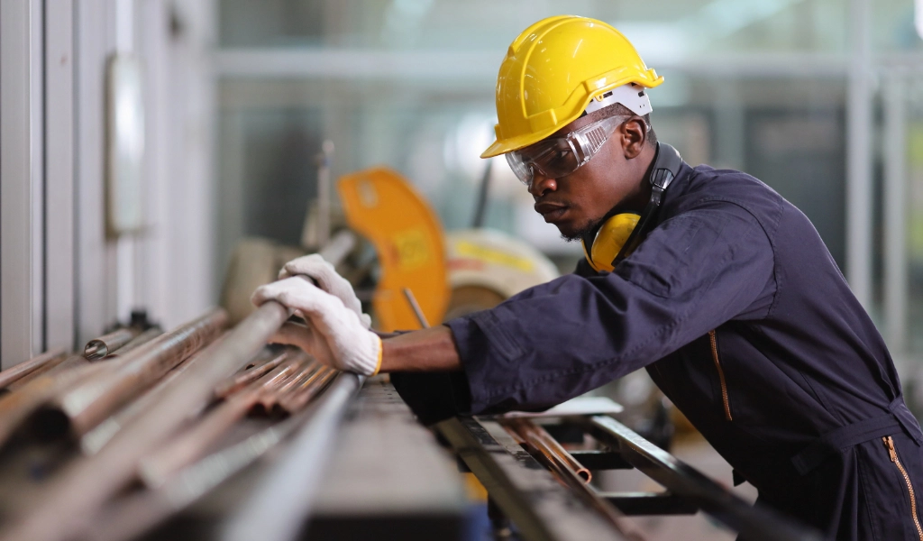 Man in a yellow hard hat measures pipe before cutting it.